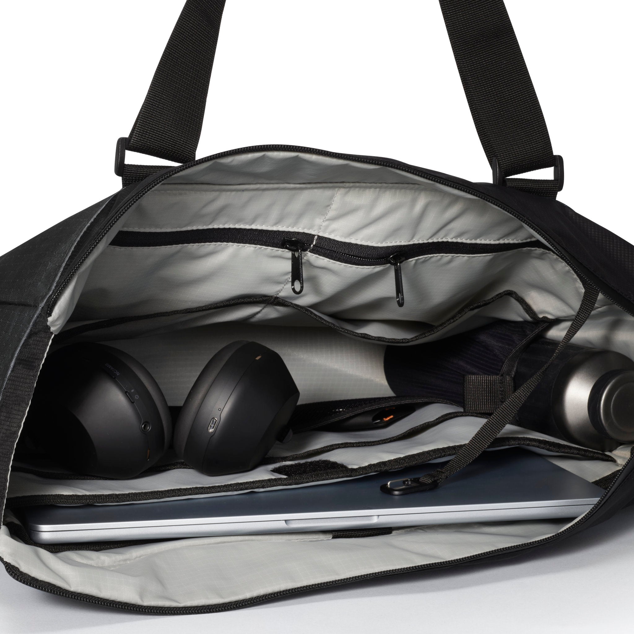 Open black duffel bag with laptop, headphones, and water bottle on a white background